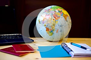 Travel items, blue notepad, pen, pc, globe on wooden background