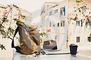 Travel items on cafe table with beautiful italian street at background. Hat, backpack, sunglasses, coffee and travel map