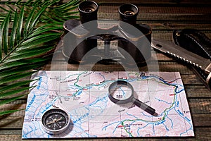 Travel kit: vintage binoculars, map, compass, hiking knife on wooden background