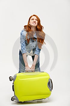 Travel and Lifestyle Concept: Young woman suffers from back pain lifting a heavy suitcase isolated on yellow background