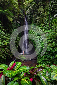 Excited Caucasian woman raising arms in front of waterfall. View from back. Leke Leke waterfall, Bali, Indonesia