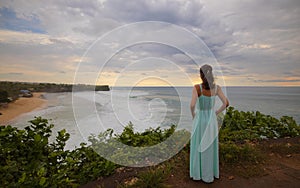 Travel lifestyle. Young woman enjoying ocean view and wearing long dress. View from back. Horizon seaview. Cliff near Balangan