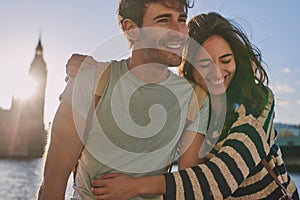 Travel, love and couple hug at big ben for happy holiday, adventure and sunset walk at river. Young, marriage and smile