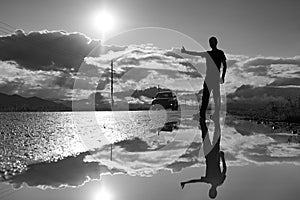 Travel man hitchhiking. Reflection in a puddle. Silhouette of man with a raised hand thumb up