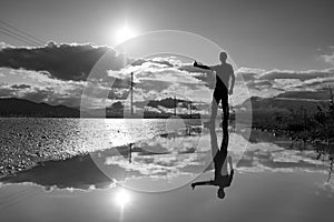 Travel man hitchhiking. Reflection in a puddle. Silhouette of man with a raised hand thumb up