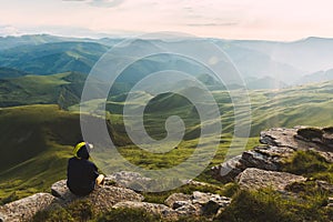 Travel man tourist sitting alone on the edge mountains over green valley adventure lifestyle extreme vacations green landscape