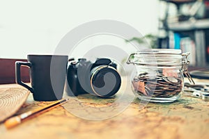 Travel money savings in a glass jar, camera, coffee cup, straw hat and pen on world map. Travel budget concept