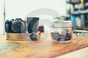 Travel money savings in a glass jar, camera, coffee cup, straw hat and pen on world map. Travel budget concept