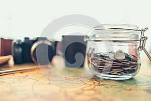 Travel money savings in a glass jar, camera, coffee cup, straw hat and pen on world map. Travel budget concept