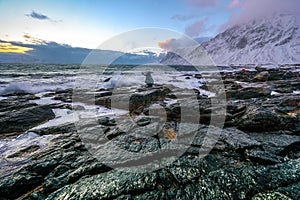 Travel photographer doing pictures in ancient stones on the shores of cold Norwegian Sea at evening time. Lofoten islands. Beautif