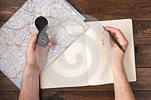 Travel planning concept. Hand writing in blank notepad with compass and map on wooden table