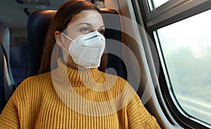Travel safely on public transport. Young business woman with KN95 FFP2 face mask looking through train window. Train passenger