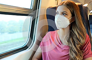 Travel safely on public transport. Young woman with KN95 FFP2 face mask looking through train window. Train passenger with