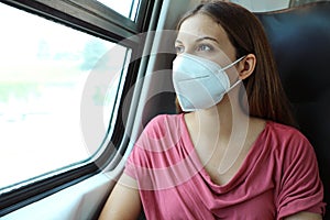 Travel safely on public transport. Young woman with KN95 FFP2 face mask looking through train window. Train passenger with