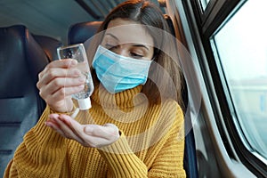 Travel safely on public transport. Young woman with surgical mask using hand sanitizer gel from dispenser. Commuter with