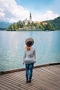 Travel Slovenia, Europe. Back view of young woman posing alone. In a white shirt with sunglasses and a cowboy hat. Bled Lake and