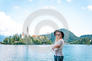 Travel Slovenia, Europe. Young girl posing alone. In a white shirt with sunglasses and a cowboy hat. Bled Lake and Alps Mountain.