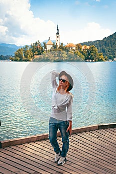 Travel Slovenia, Europe. Young girl posing alone. In a white shirt with sunglasses and a cowboy hat. Bled Lake and Alps Mountain.