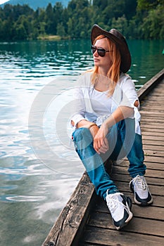 Travel Slovenia, Europe. Young girl posing alone. In a white shirt with sunglasses and a cowboy hat. Bled Lake and Alps Mountain.