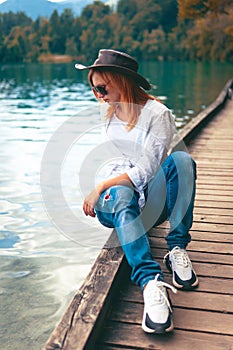 Travel Slovenia, Europe. Young girl posing alone. In a white shirt with sunglasses and a cowboy hat. Bled Lake and Alps Mountain.