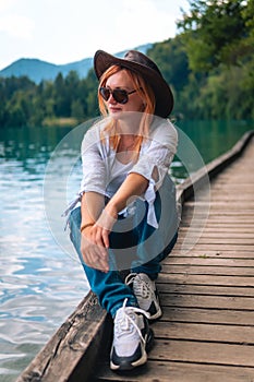 Travel Slovenia, Europe. Young girl posing alone. In a white shirt with sunglasses and a cowboy hat. Bled Lake and Alps Mountain.