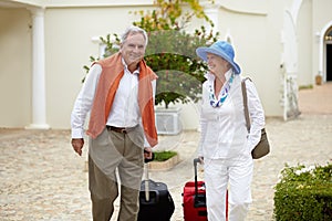 Travel, suitcase and elderly couple walking on vacation in a holiday location happy in retirement together by a hotel