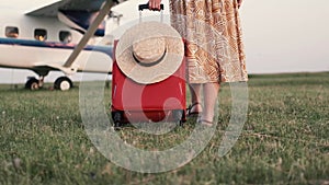 Travel suitcase on wheels in hand and female legs in sandals going to the plane