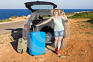 Travel, summer holidays and vacation concept - Young woman with suitcases on car trip.