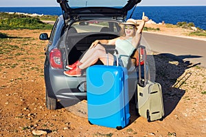 Travel, summer holidays and vacation concept - Young woman with suitcases on car trip. She is sitting in car back and