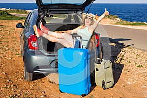 Travel, summer holidays and vacation concept - Young woman with suitcases on car trip. She is sitting in car back and