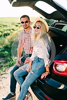 Travel, summer vacation, road trip, leisure and people concept. Happy couple drinking coffee from disposable cups sitting on trunk