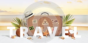 Travel text front of retro suitcase with travel stickers on beach surrounded by palm leaves, coconuts and shells