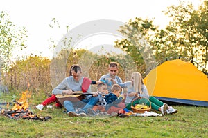 Travel, tourism, hike, picnic and people concept - group of happy friends with tent and drinks playing guitar at camping