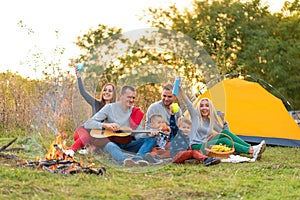 Travel, tourism, hike, picnic and people concept - group of happy friends with tent and drinks playing guitar at camping