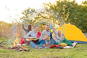 Travel, tourism, hike, picnic and people concept - group of happy friends with tent and drinks playing guitar at camping