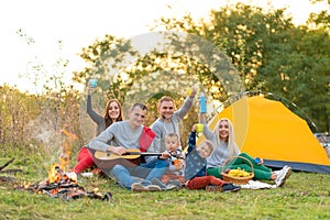 Travel, tourism, hike, picnic and people concept - group of happy friends with tent and drinks playing guitar at camping