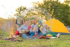 Travel, tourism, hike, picnic and people concept - group of happy friends with tent and drinks playing guitar at camping