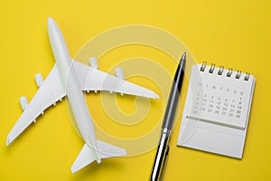 Travel, tourism, holiday or vacation planning concept, small white clean calendar with black pen and toy airplane on vibrant yell