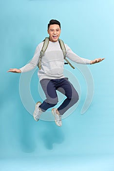 Travel, tourism and people concept - happy smiling young man with backpack jumping in air over grey background