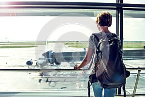 Travel tourist standing with luggage watching at airport window.