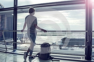 Travel tourist standing with luggage watching at airport window.