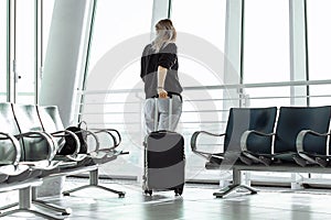 Travel tourist woman standing with luggage watching at airport window. Unrecognizable woman. Travel, lifestyle.