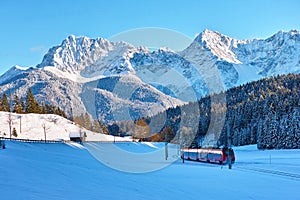 Red train in snow-covered Alpine scenery by blue sky