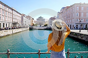 Travel in Trieste, Italy. Back view of pretty girl holding hat looking at Sant Antonio Taumaturgo church on Grand Canal in Trieste