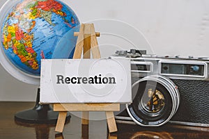 Travel and vacation concept image,word RECREATION and with easel ,globe and vintage camera layout on wooden desk