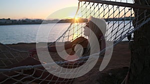 Travel and vacation concept - Woman relaxing on hammock on the beach at sunset