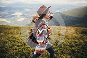 travel and wanderlust concept. stylish traveler hipster girl holding hat, with backpack and windy hair, walking in mountains in c photo