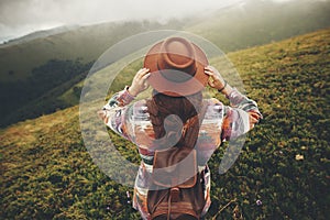 travel and wanderlust concept. stylish traveler hipster girl holding hat, with backpack and windy hair, walking in mountains in c photo