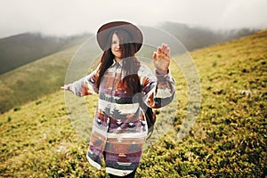 travel and wanderlust concept. stylish traveler hipster girl holding hat, with backpack and windy hair, walking in mountains in c