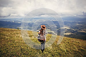 travel and wanderlust concept. stylish traveler hipster girl holding hat, with backpack and windy hair, walking in mountains in c